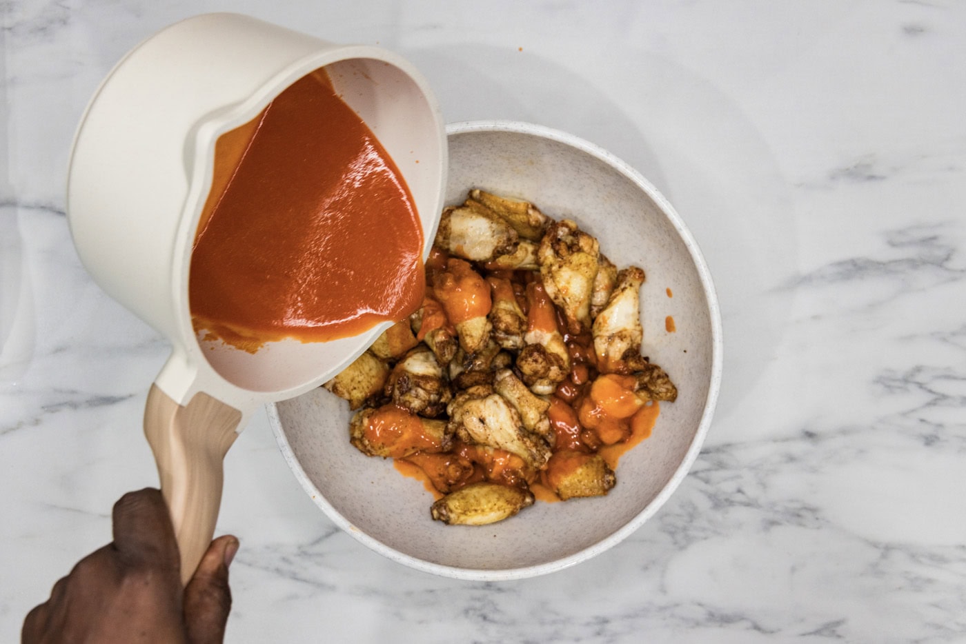 pouring buffalo sauce over chicken wings in a bowl