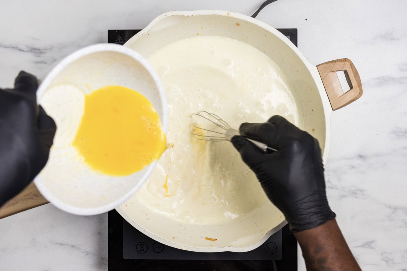 slowly pouring eggs into cream mixture in a skillet using a whisk