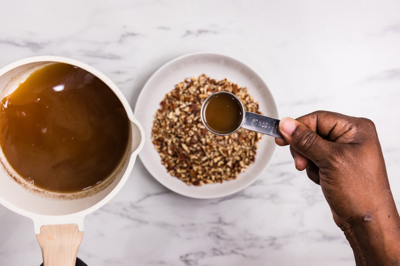 hand adding 1/3 cup of bourbon sauce to chopped pecans