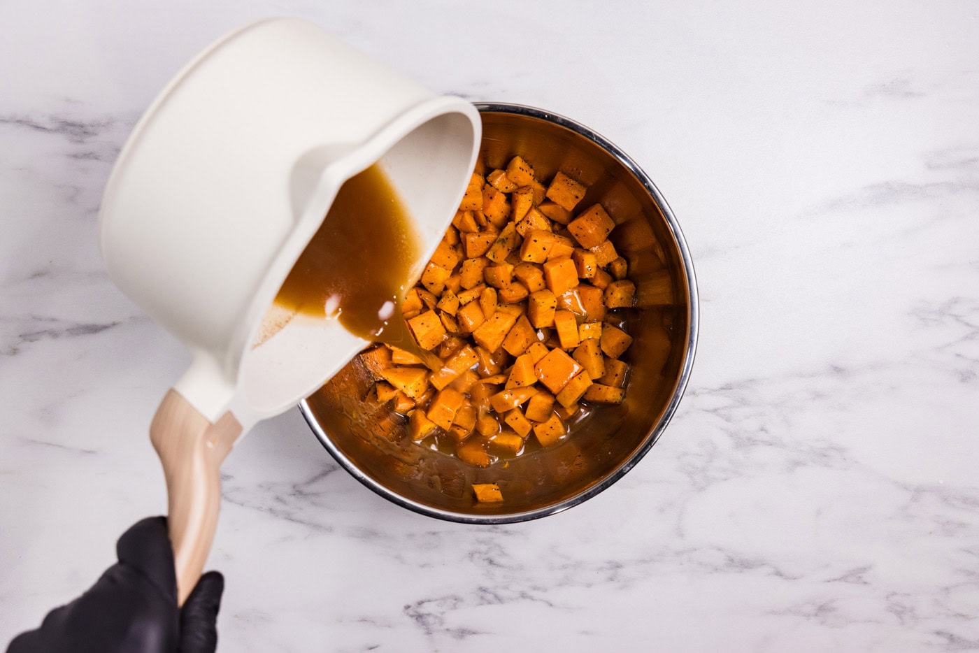 pouring sauce over cubed sweet potatoes in a bowl