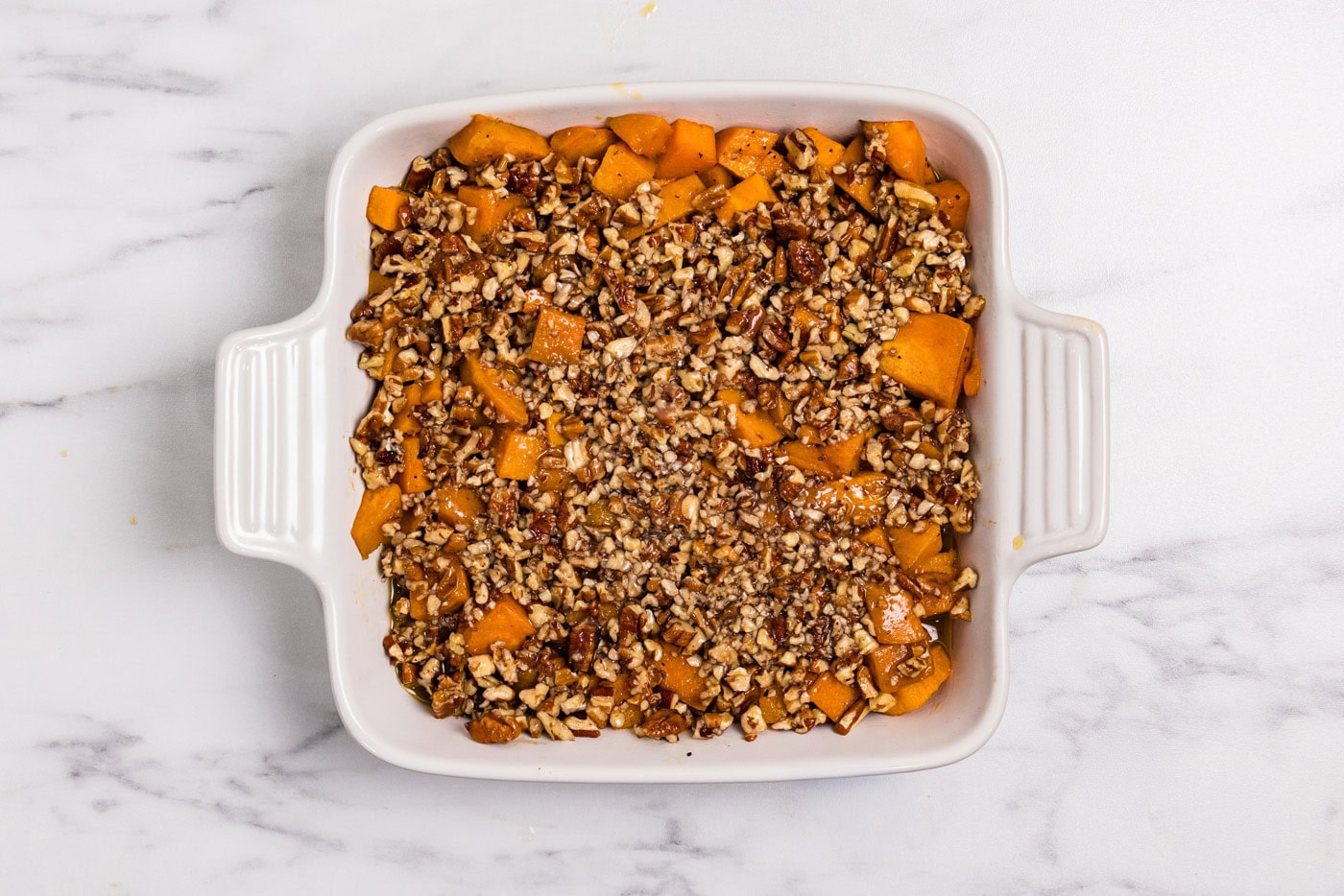 bourbon sweet potatoes in a baking dish topped with chopped pecans