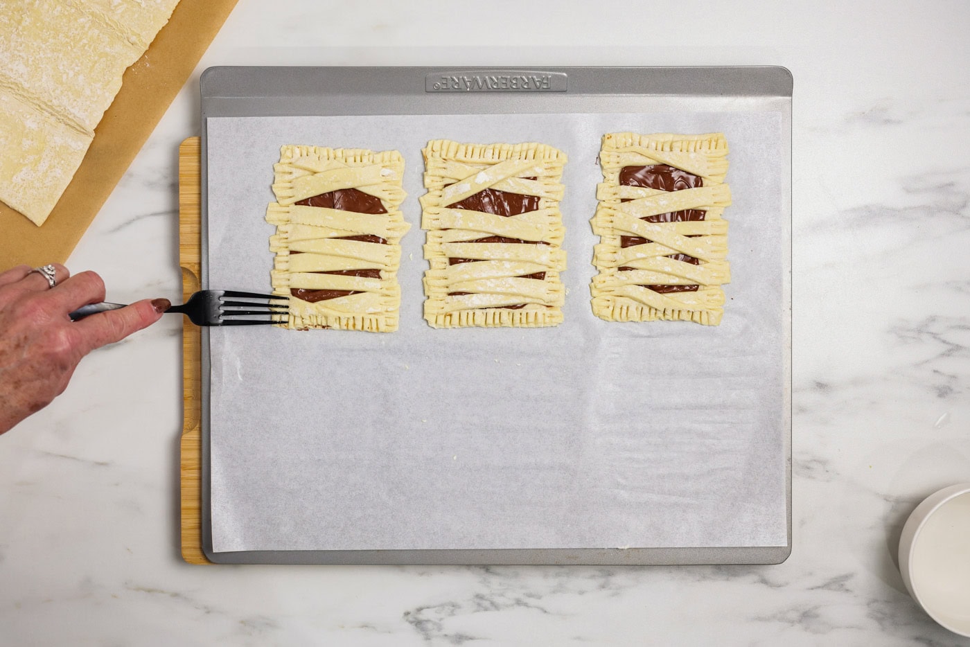 Fork pressing into mummy hand pies to seal the edges