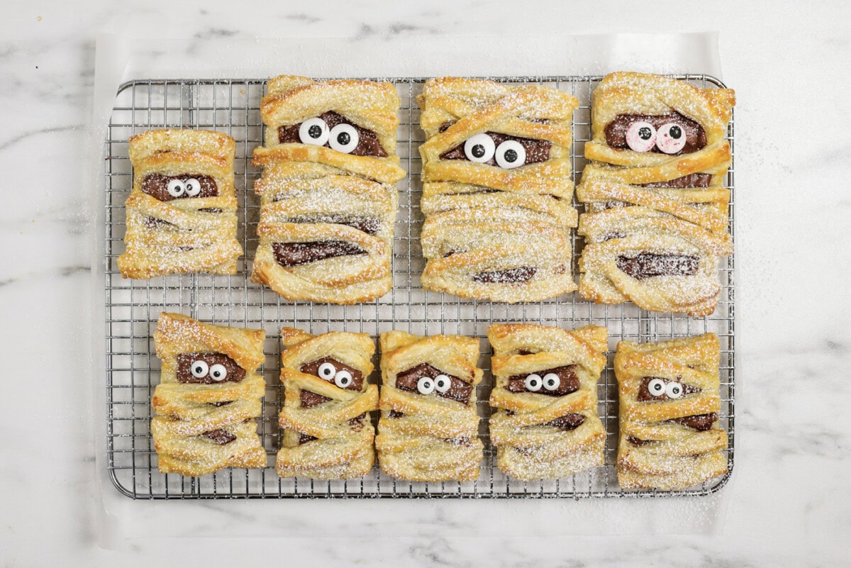 powdered sugar dusted over mummy hand pies on a wire cooling rack
