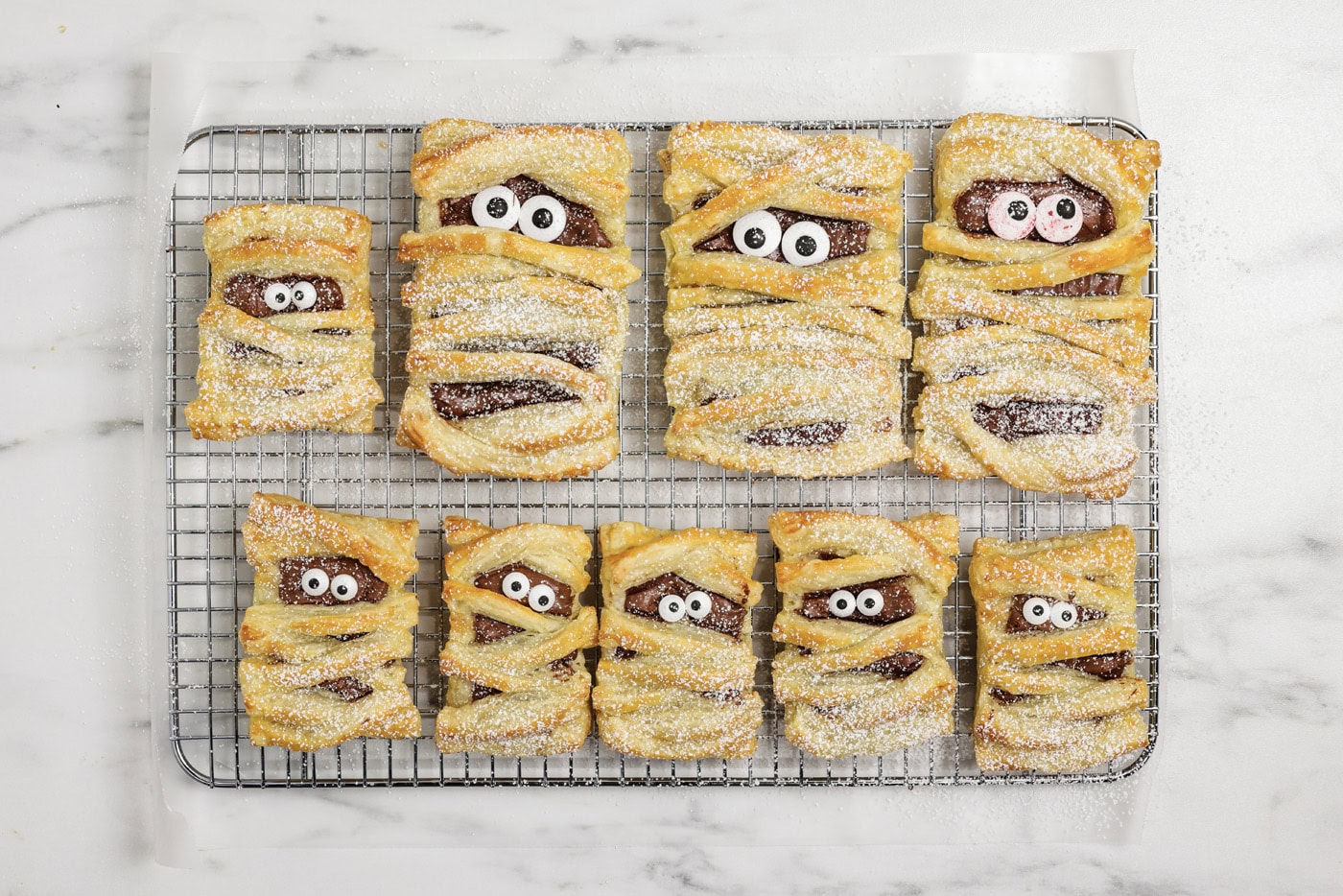 powdered sugar dusted over mummy hand pies on a wire cooling rack