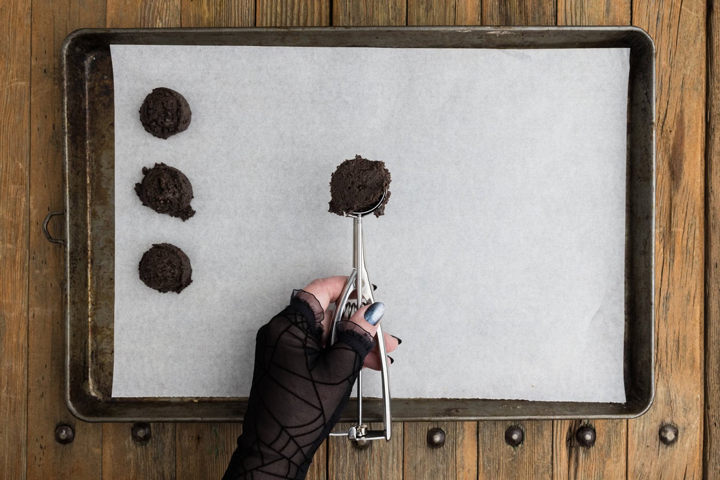 Tablespoon scoop of Oreo truffle mixture held over a parchment lined baking sheet