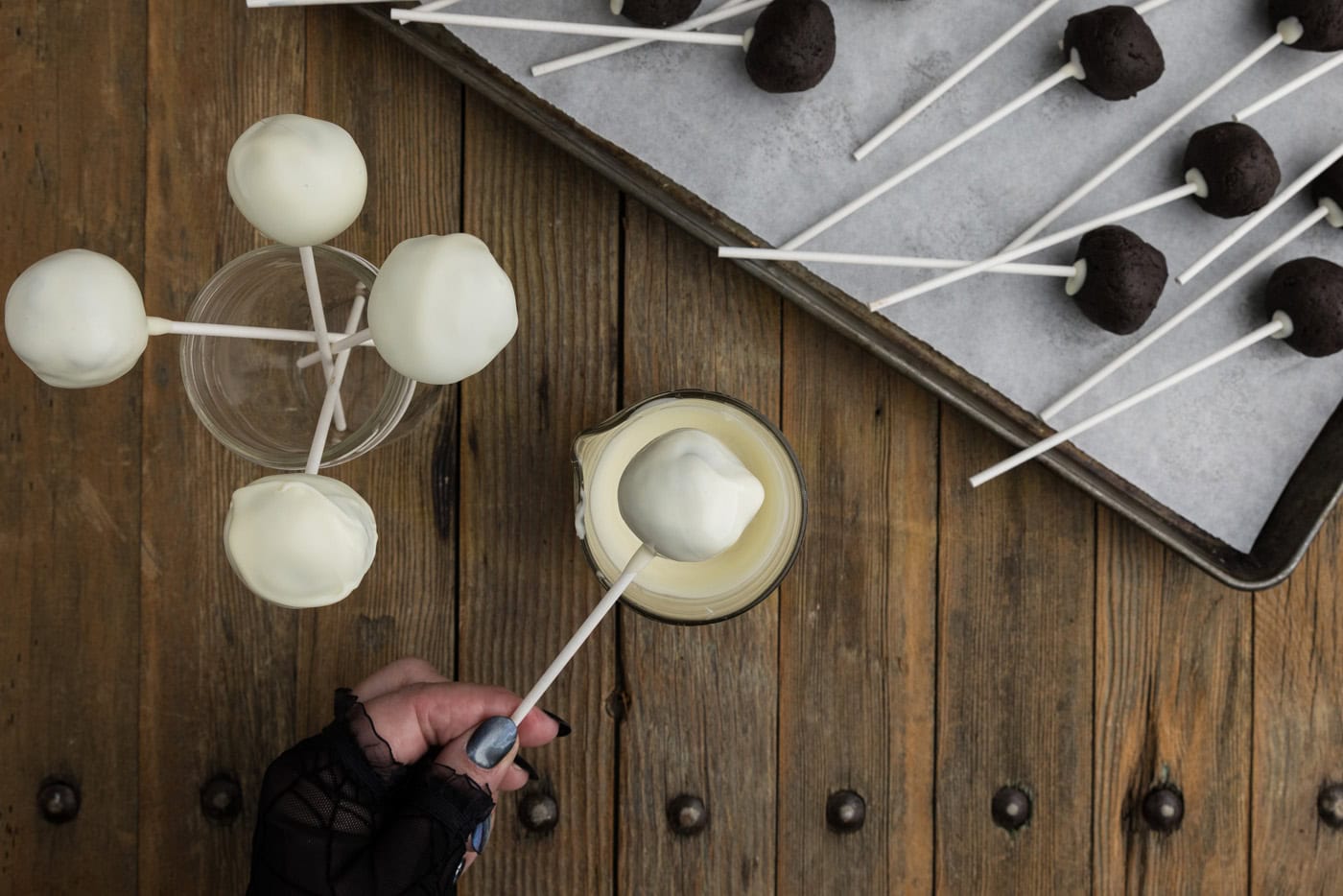 Hand dipping an Oreo truffle into white chocolate coating holding on to the lollipop stick