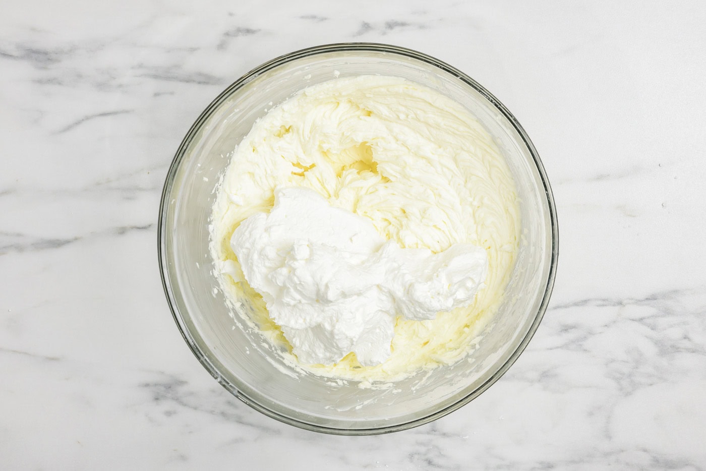 adding whipped cream to a bowl of mascarpone and cream cheese mixture