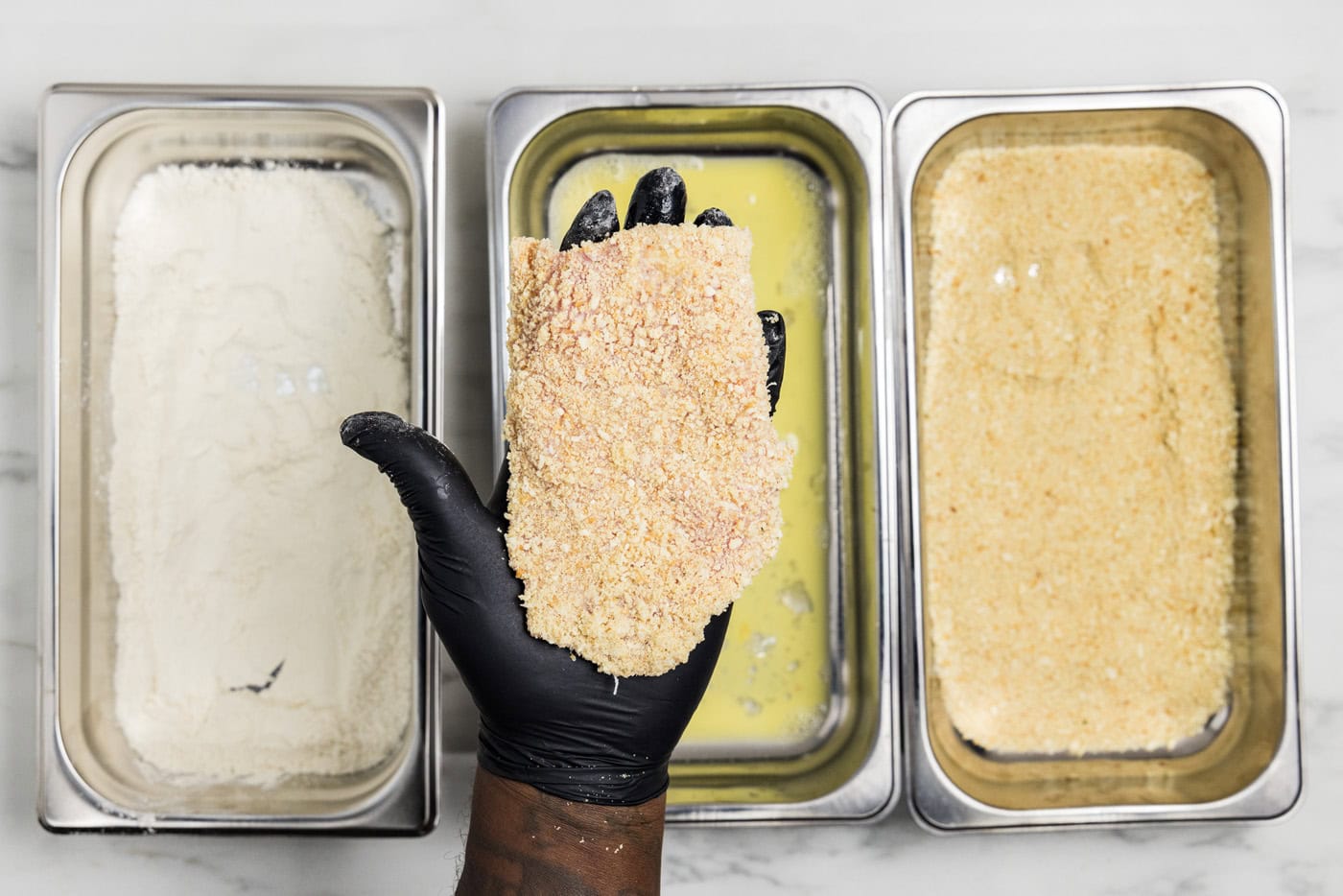 gloved hand holding panko breaded veal cutlet