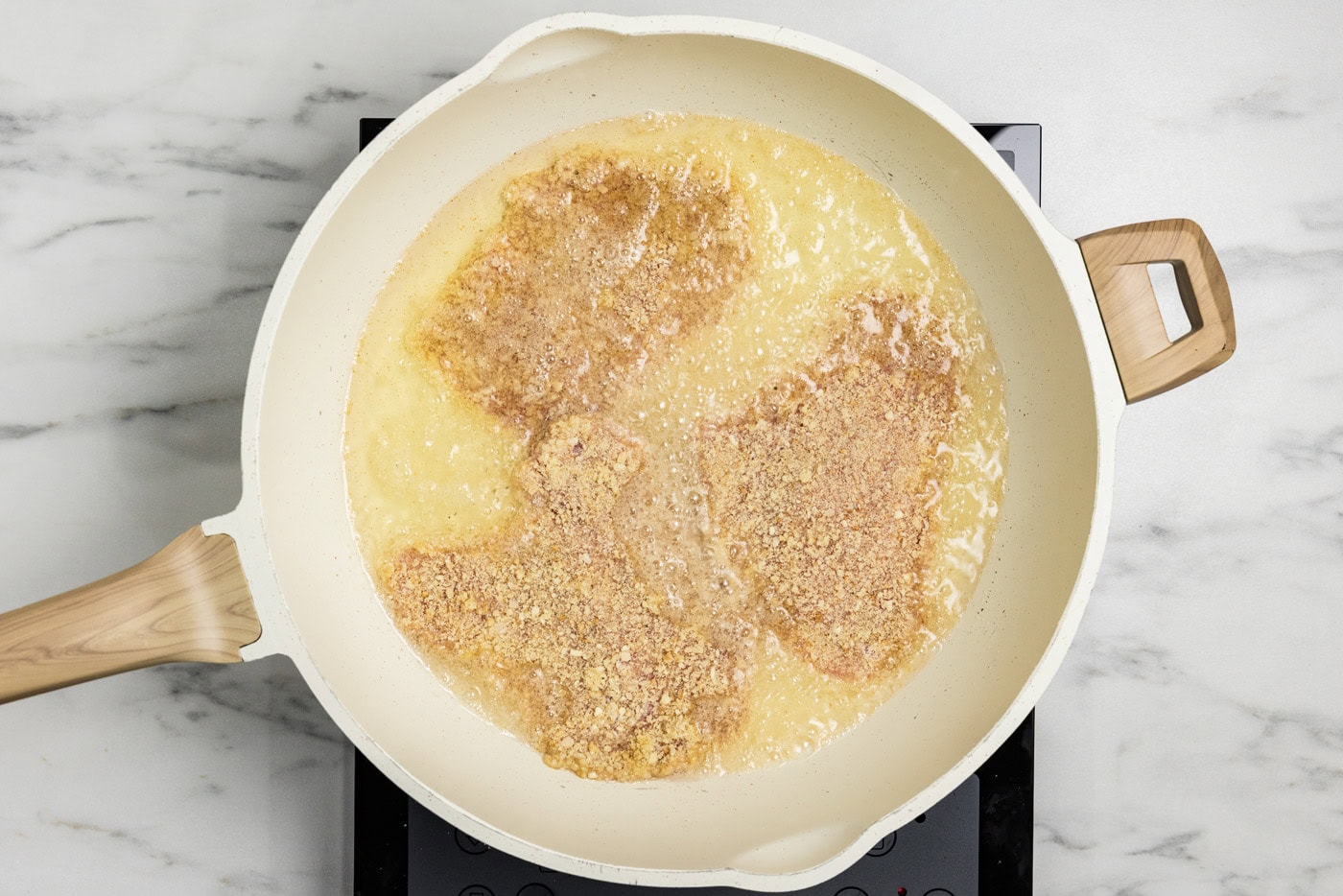 frying panko breaded veal cutlets in a skillet with oil