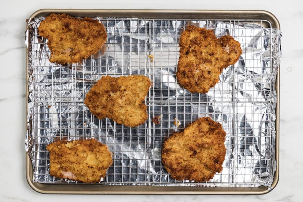 cooked breaded veal cutlets on a wire rack over a baking sheet