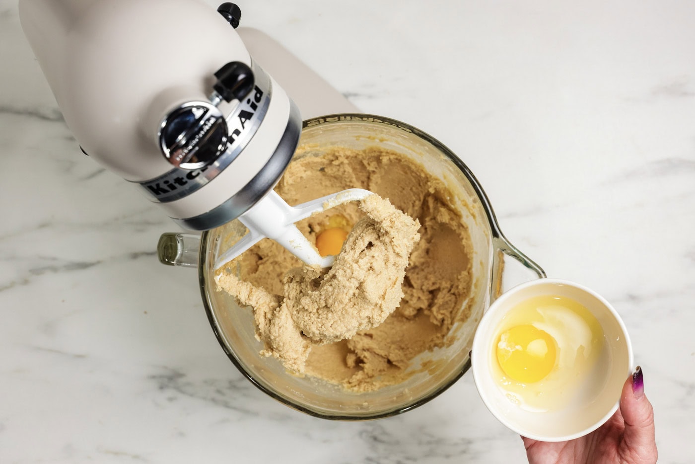 adding egg to stand mixer bowl with butter and sugar mixture