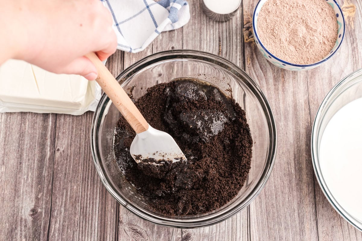 Spoon stirring Oreo cookie crumbs and melted butter in a mixing bowl
