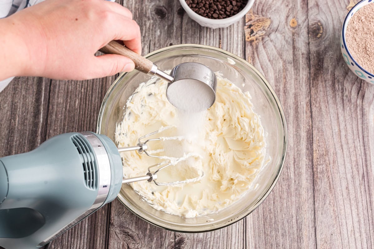 Sugar being added to a bowl of beaten cream cheese and milk