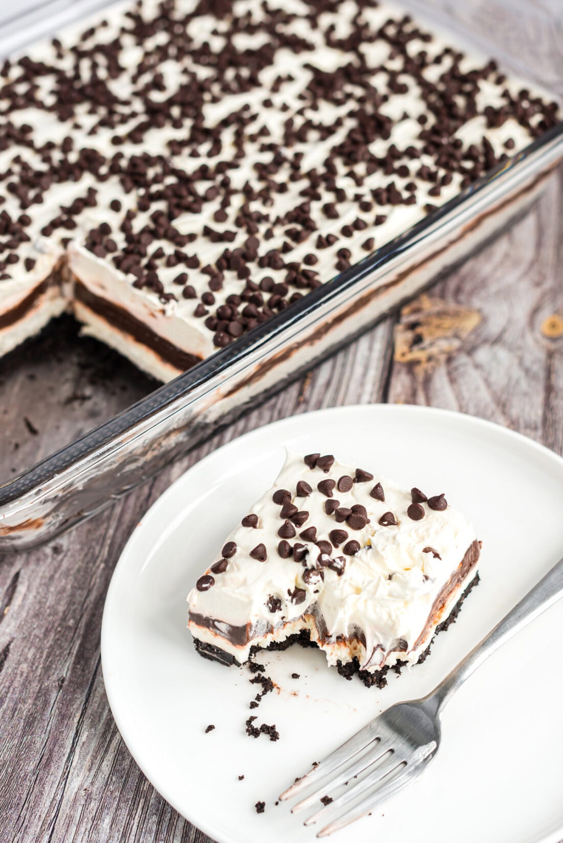Slice of Chocolate Lasagna on a plate with a pan of Chocolate Lasagna behind it