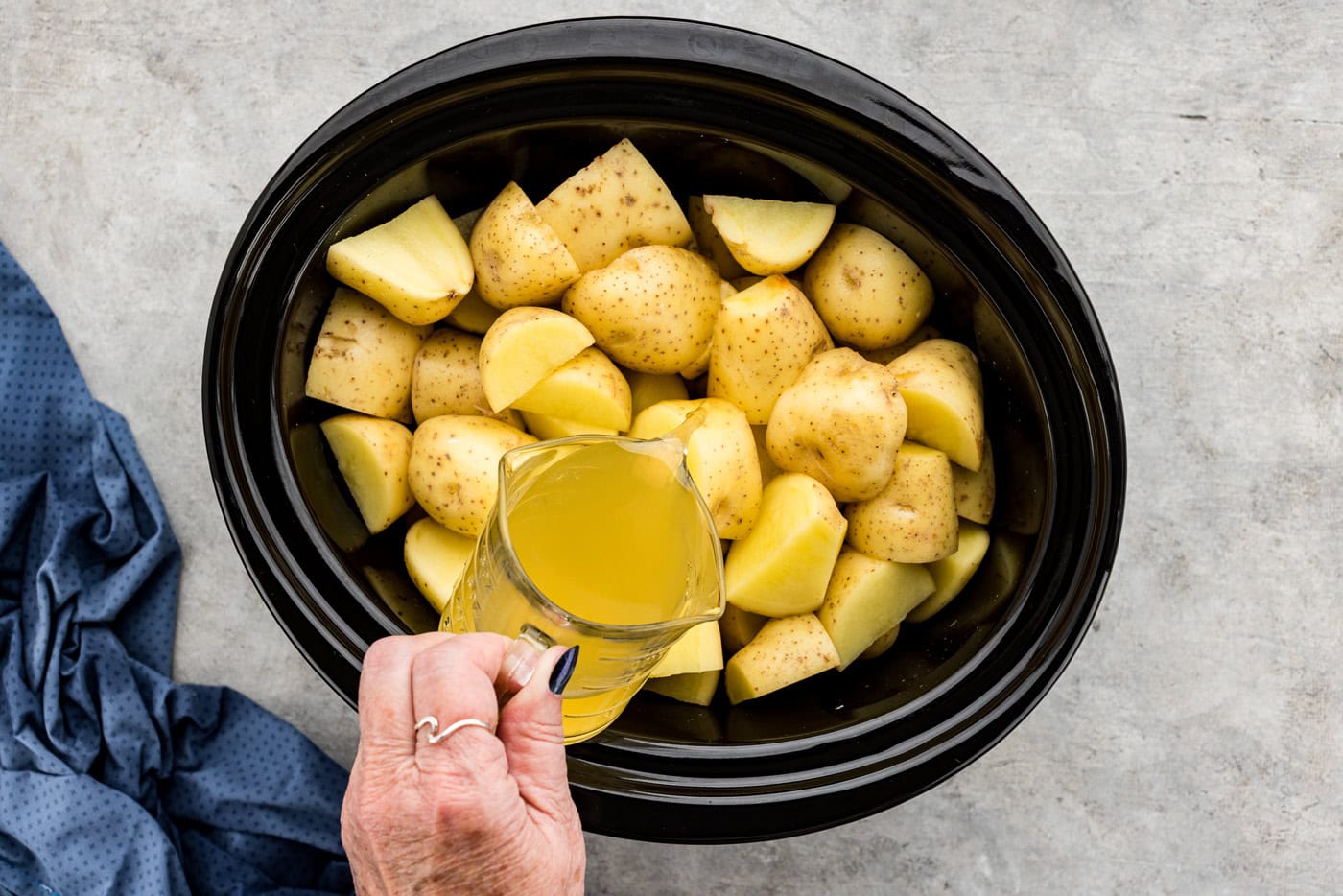 pouring chicken broth into crockpot with cubed yukon gold potatoes