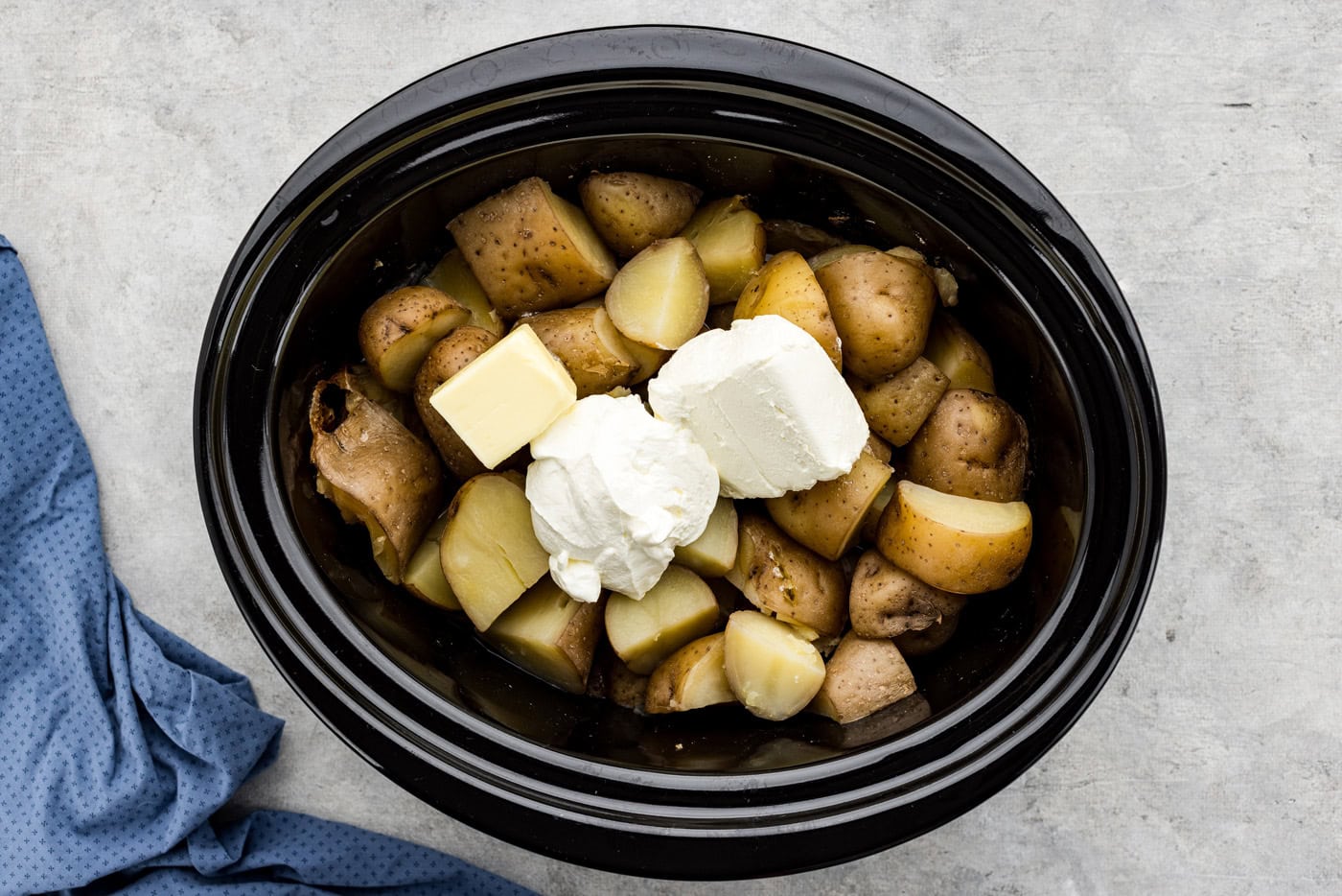 cream cheese, sour cream, and butter on top of cooked potatoes in a crockpot