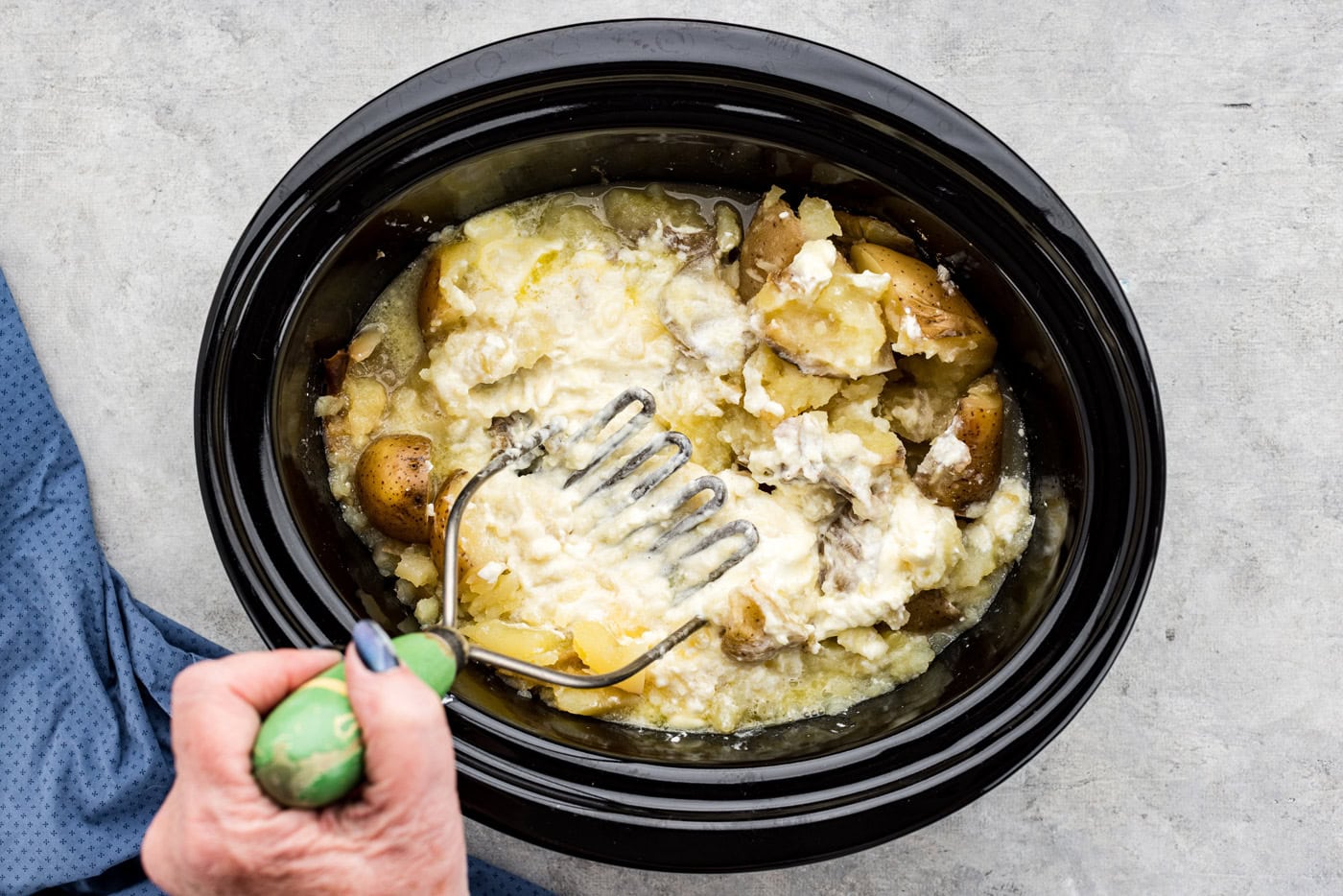 hand using a potato masher to mash ingredients together in a crockpot