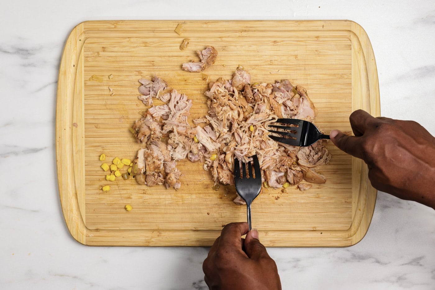 Shredding chicken with two forks on a cutting board
