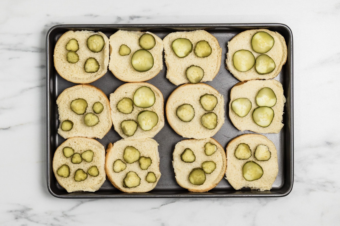 sliders buns on a baking sheet with pickles