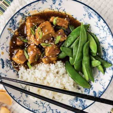 Close up photo of a bowl of Instant Pot Honey Garlic Chicken with rice and sugar snap peas