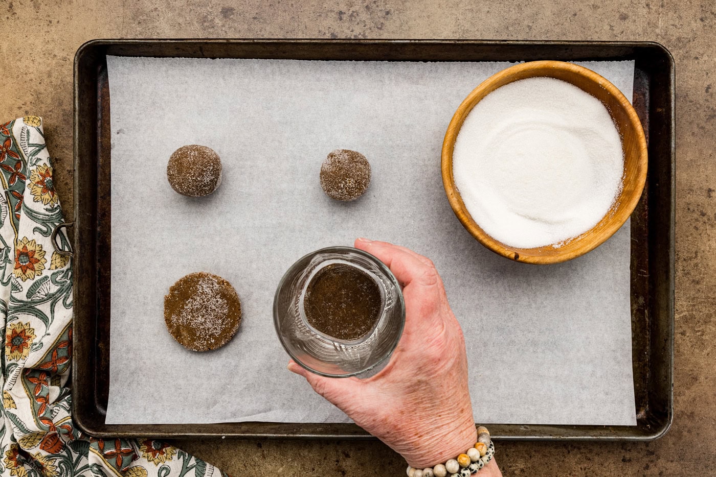 using a glass to flatten cookie dough balls on a baking sheet