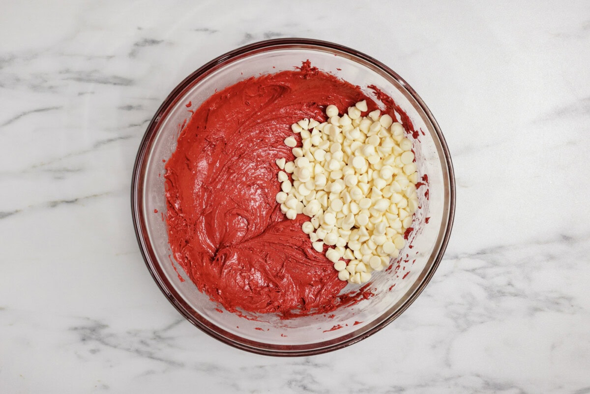 white chocolate chips added to red velvet cake batter in a mixing bowl