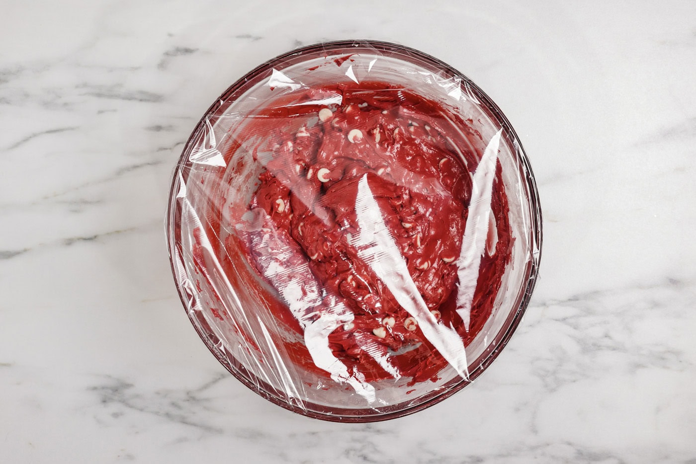 plastic wrap covering a bowl of red velvet cake cookie dough