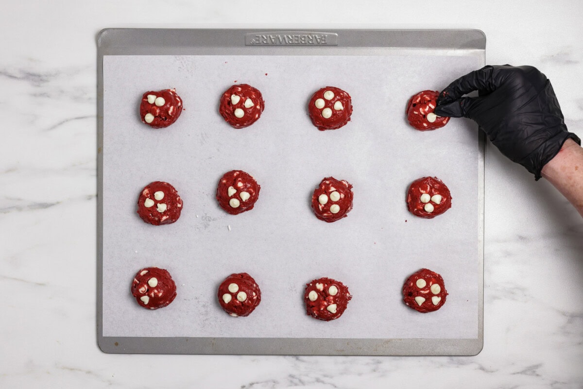 hand dotting red velvet cookie dough balls with white chocolate chips on a baking sheet