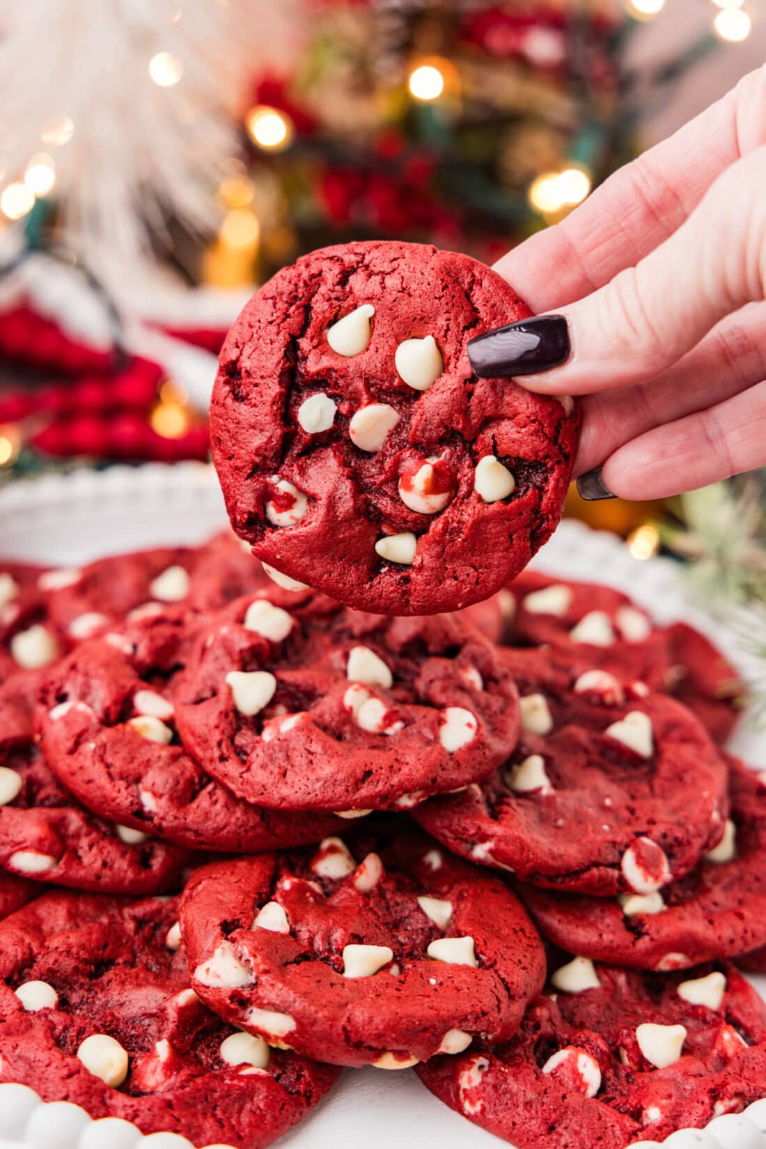 Hand holding a Red Velvet Cake Mix Cookie over a plate of more cookies