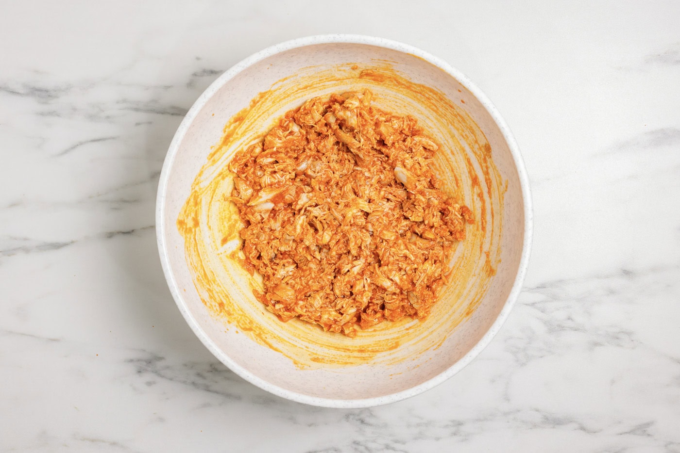 Shredded chicken in a bowl mixed with buffalo sauce