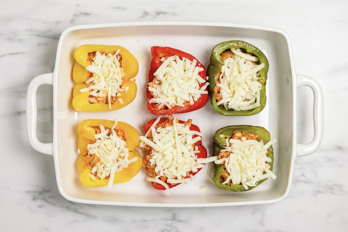 Shredded mozzarella cheese on top of buffalo chicken stuffed peppers