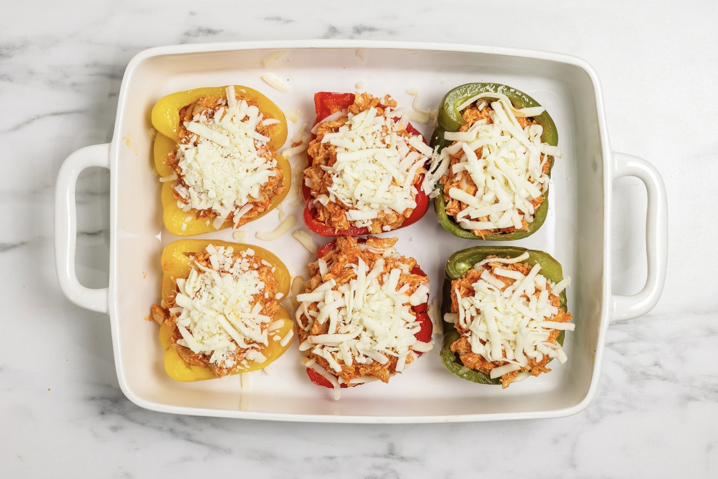 Mozzarella cheese on top of buffalo chicken stuffed peppers in a baking dish