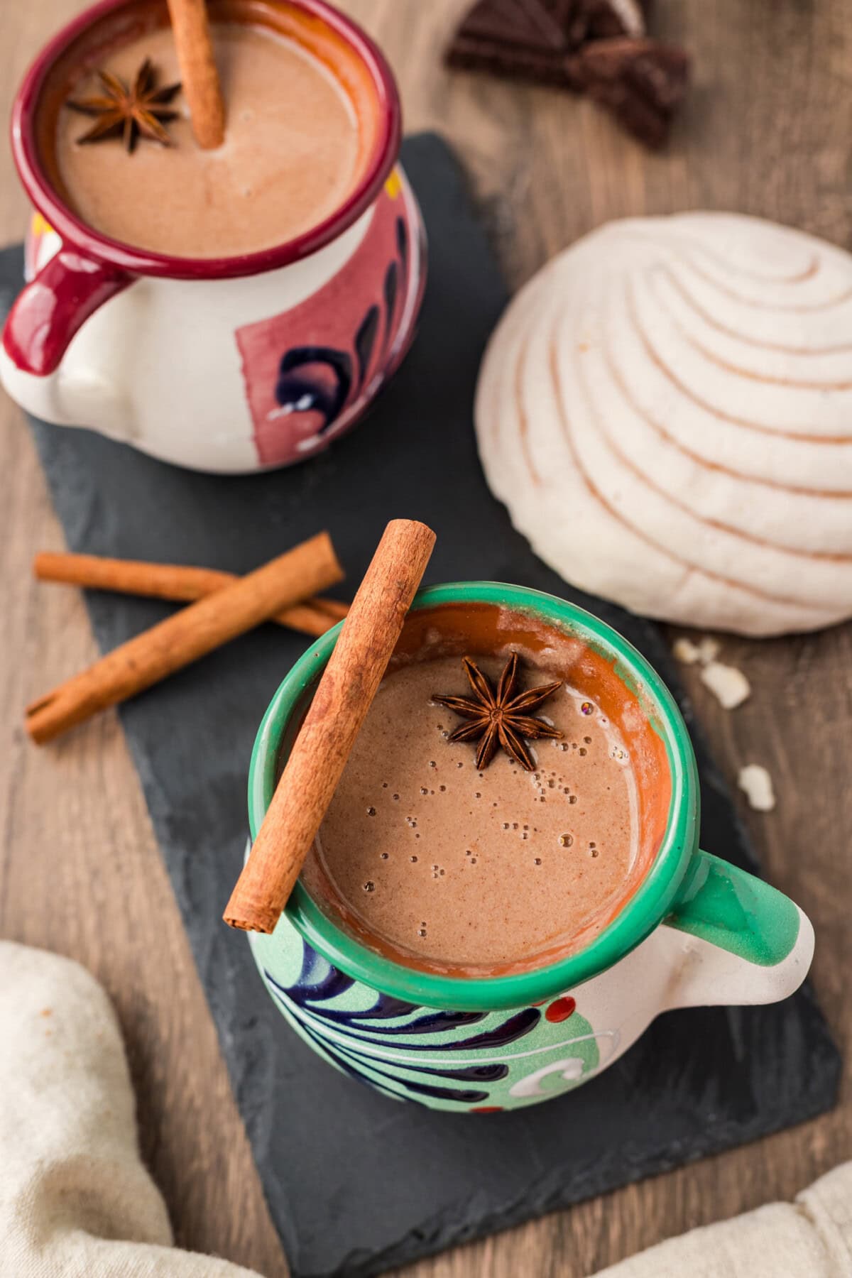 Two mugs of Champurrado with a cinnamon stick and star anise resting on top