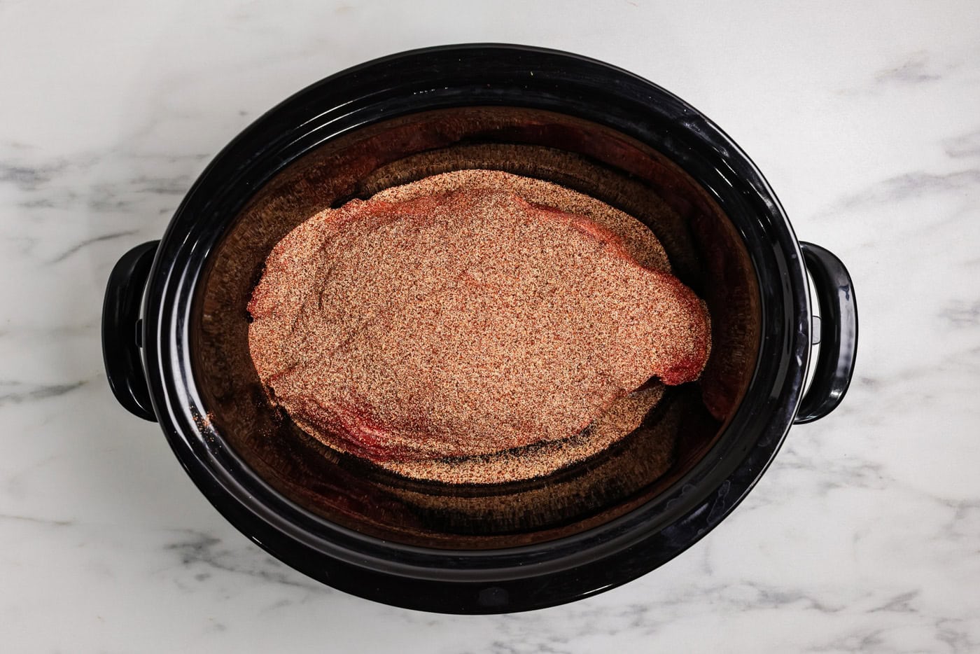 chuck roast in a slow cooker covered with seasonings