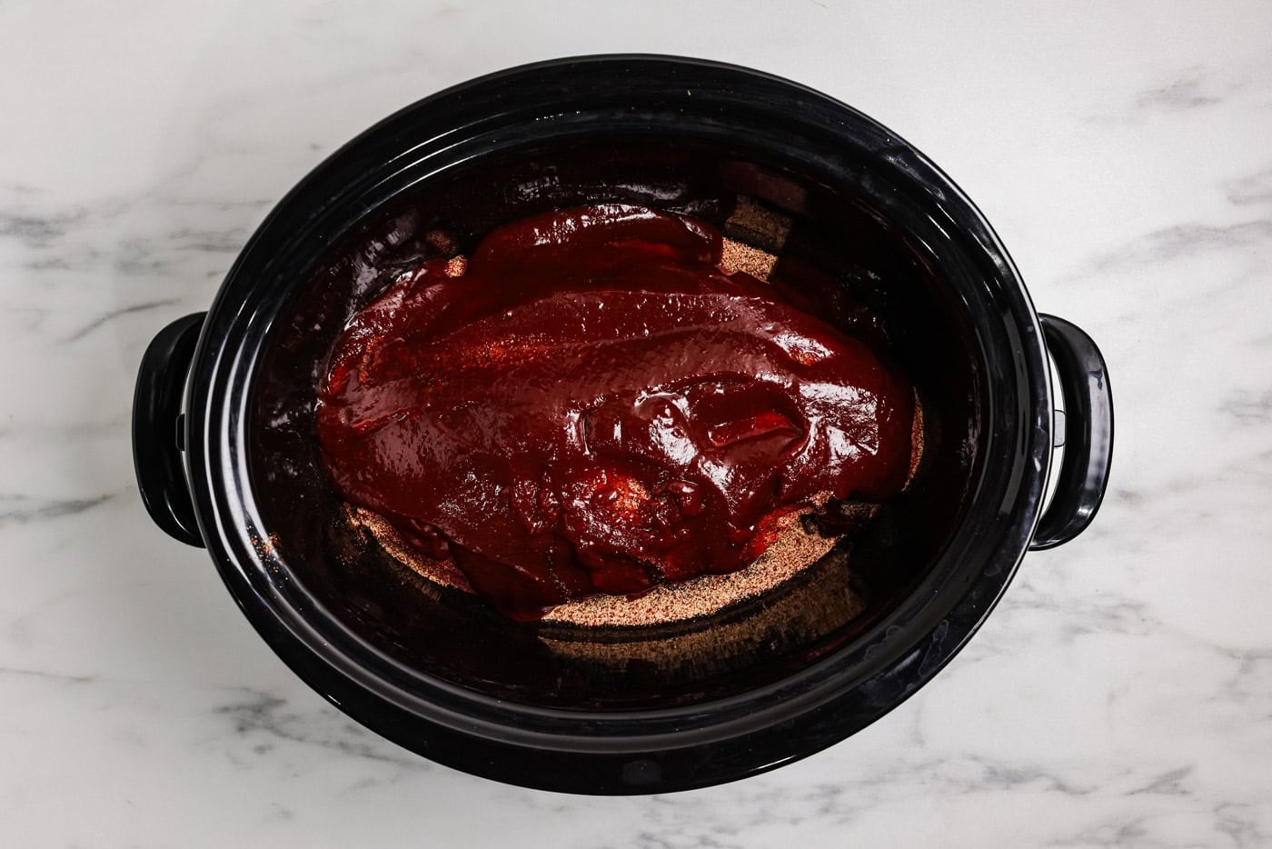 barbecue sauce poured over chuck roast and seasonings in a crockpot