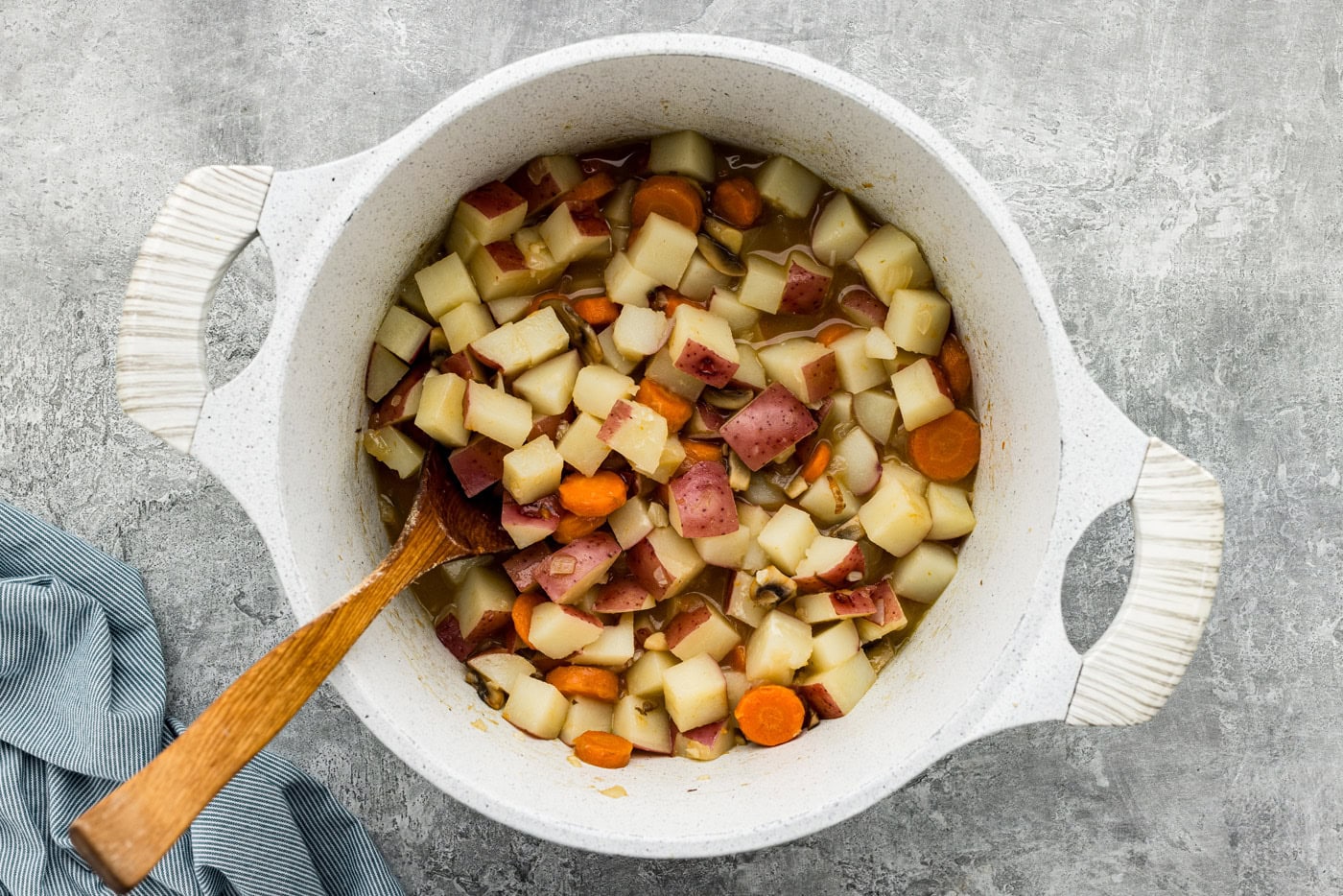 carrots, potatoes, mushrooms, and garlic in a Dutch oven with a wooden spoon