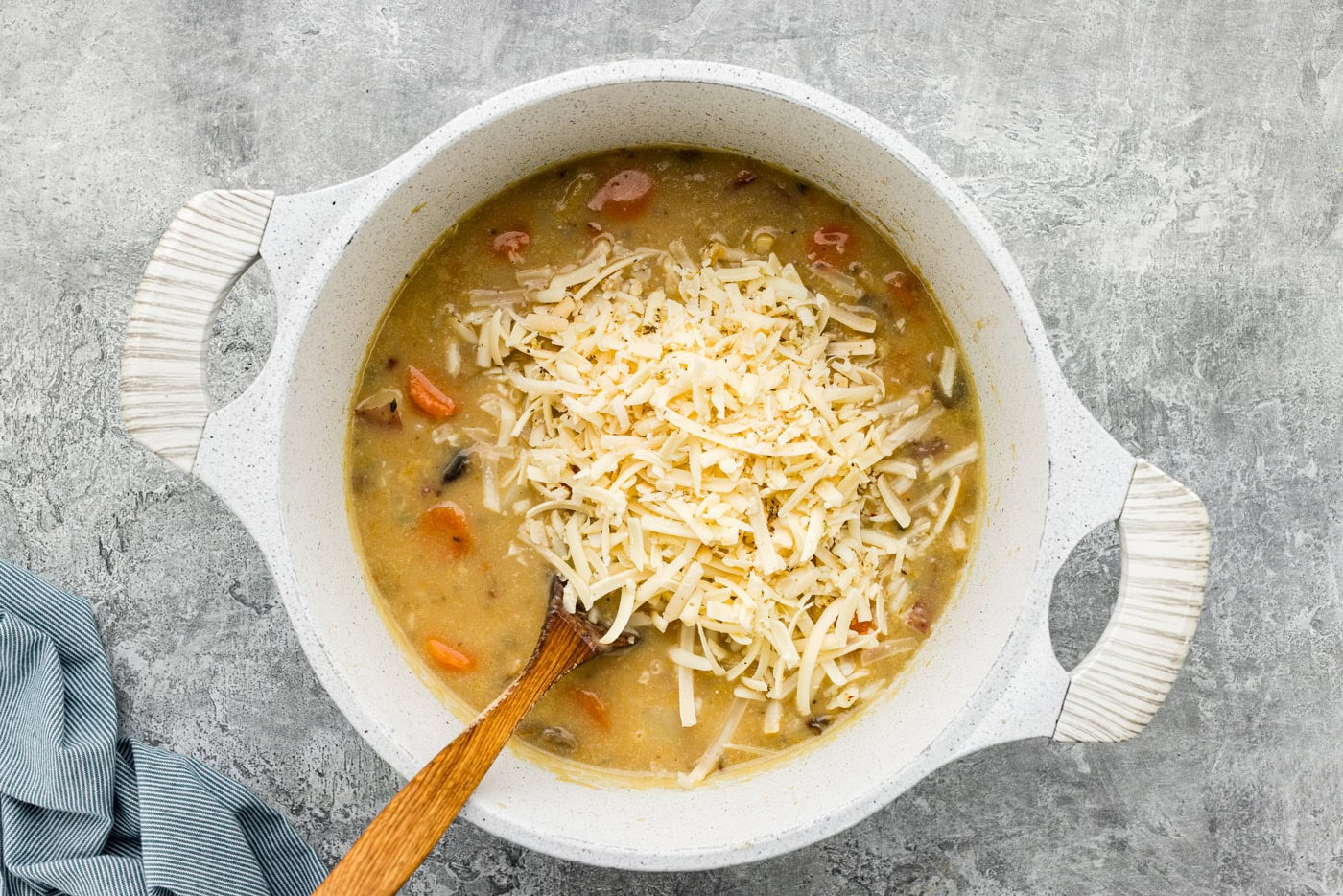 shredded cheese added to garlic potato soup in a Dutch oven