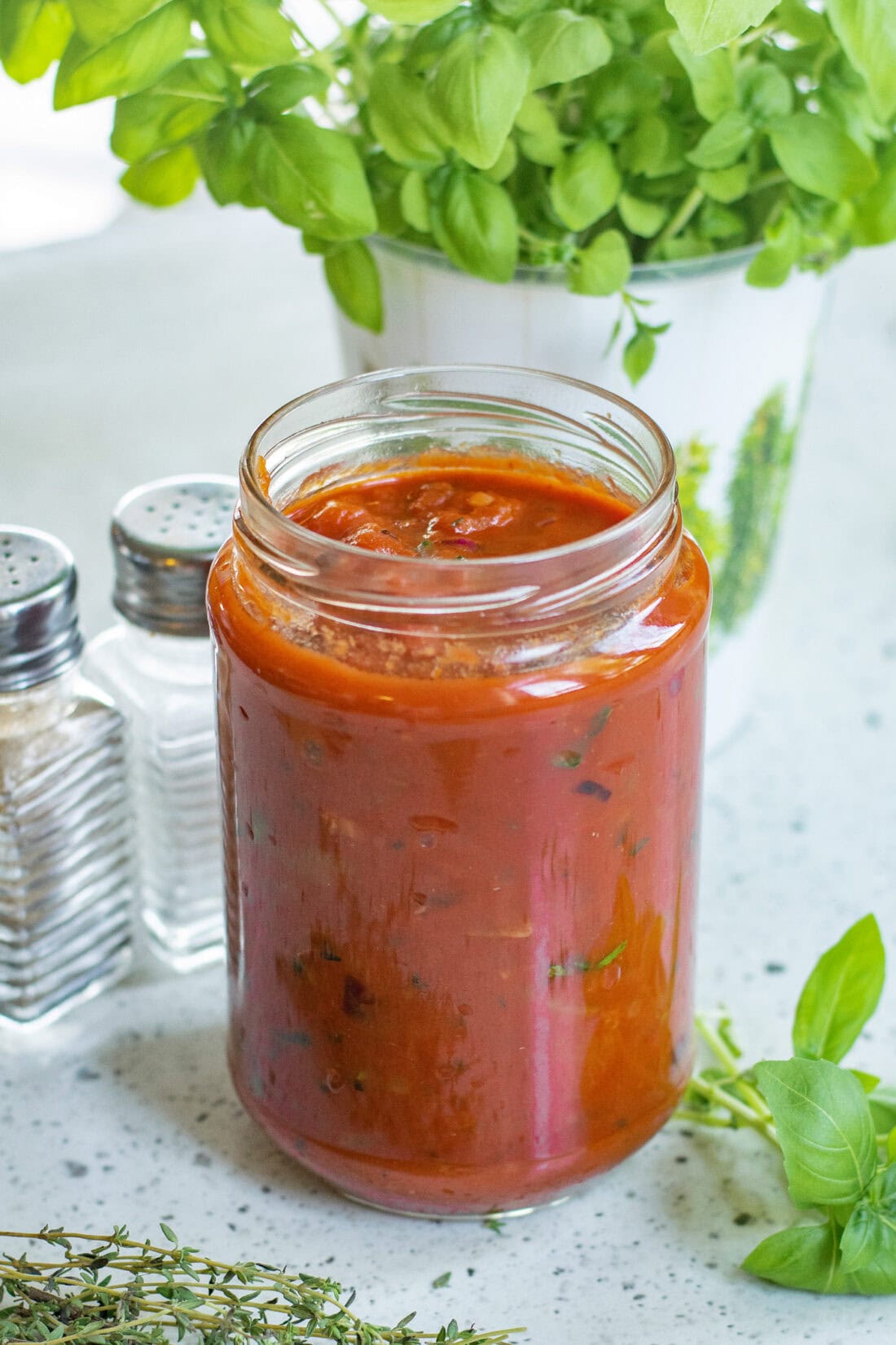 Jar of Marinara Sauce with fresh herbs around it