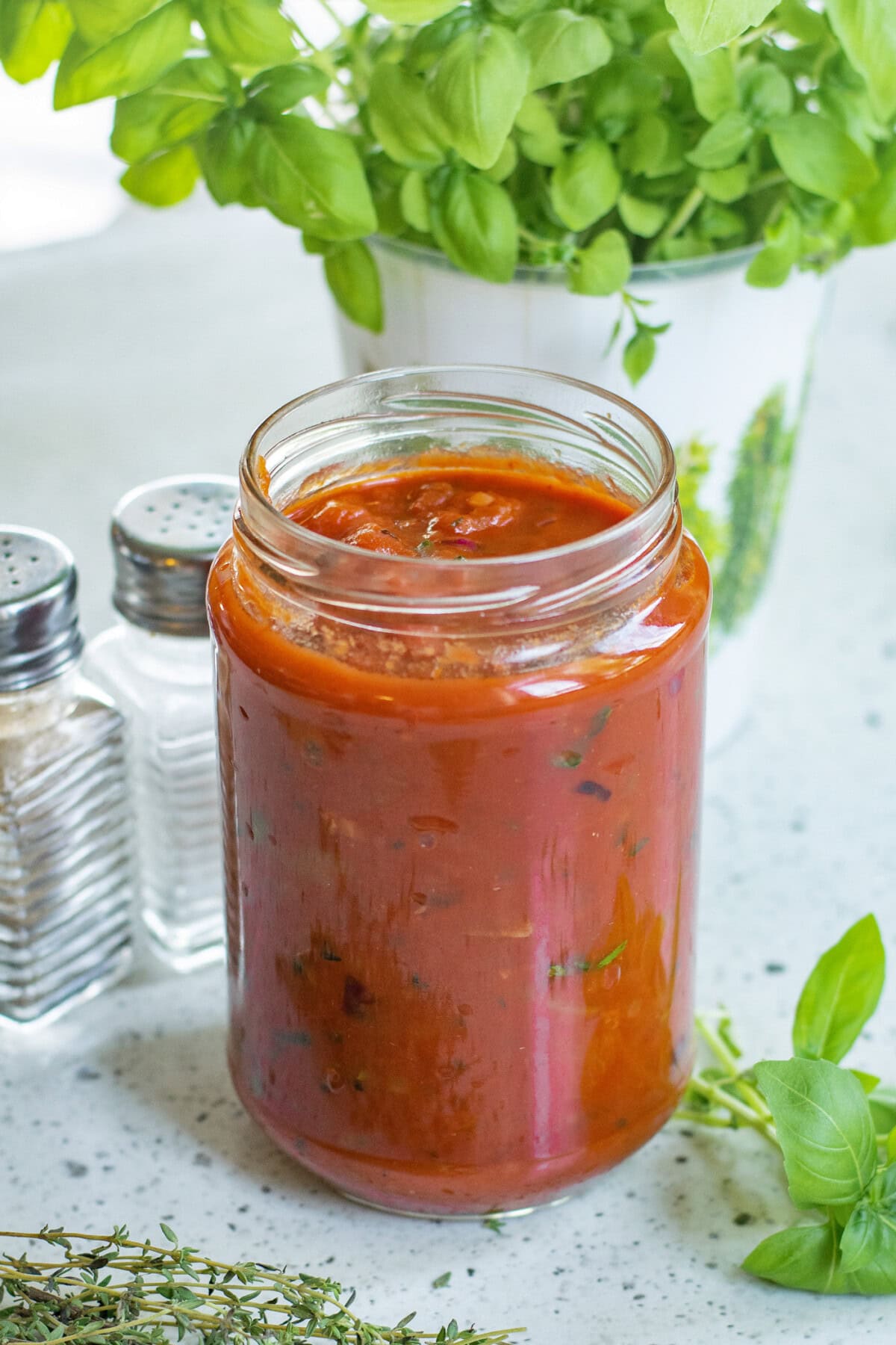 Jar of Marinara Sauce with fresh herbs around it