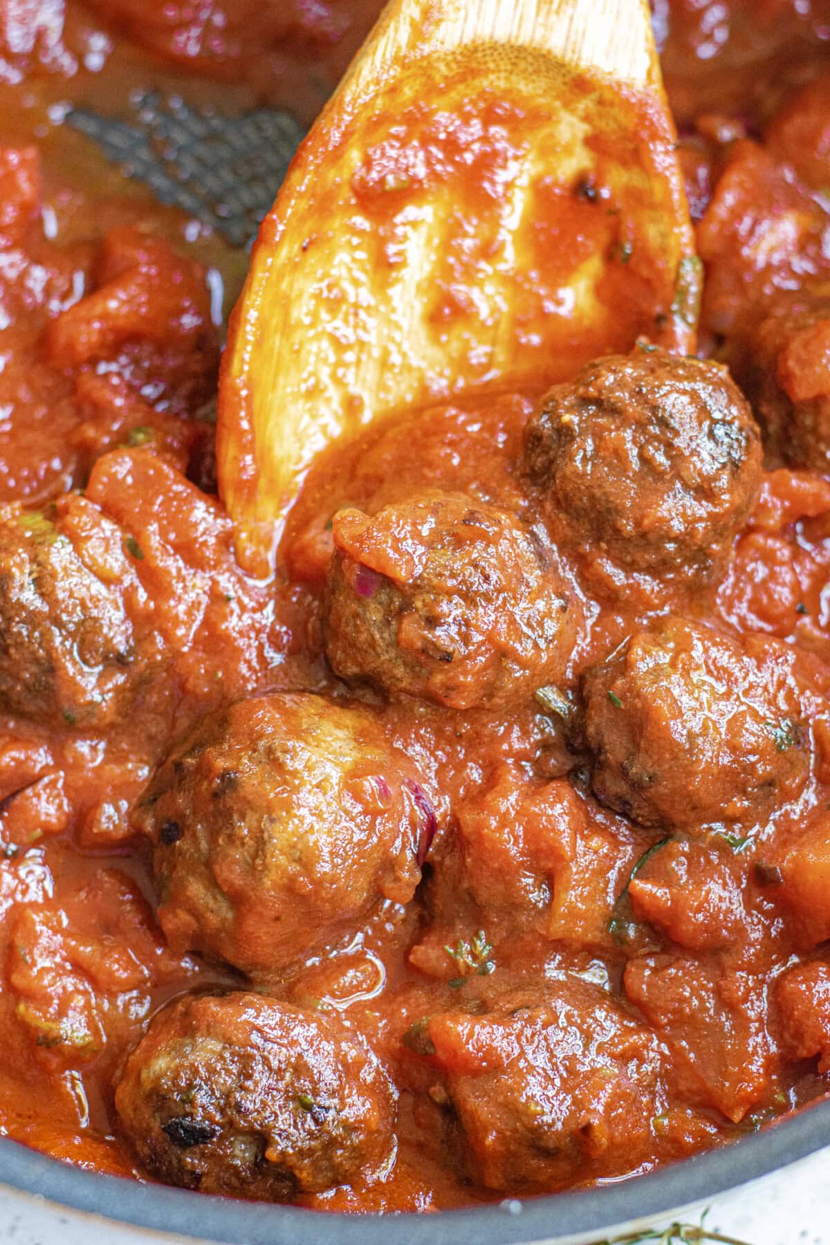 Spoon stirring a skillet of meatballs covered in Marinara Sauce