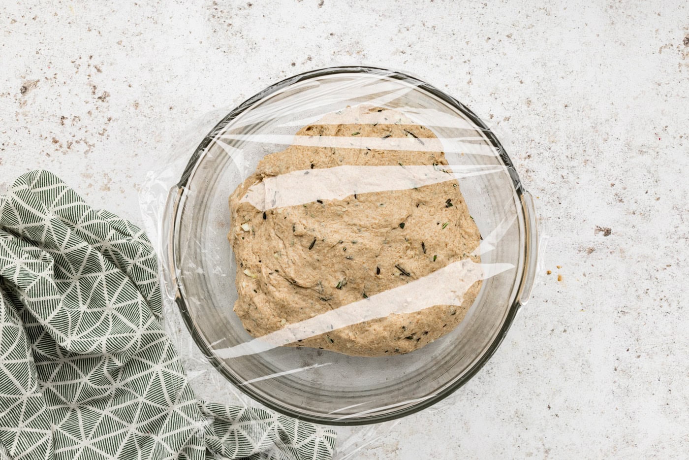 rustic rosemary garlic bread dough in a bowl covered with plastic wrap