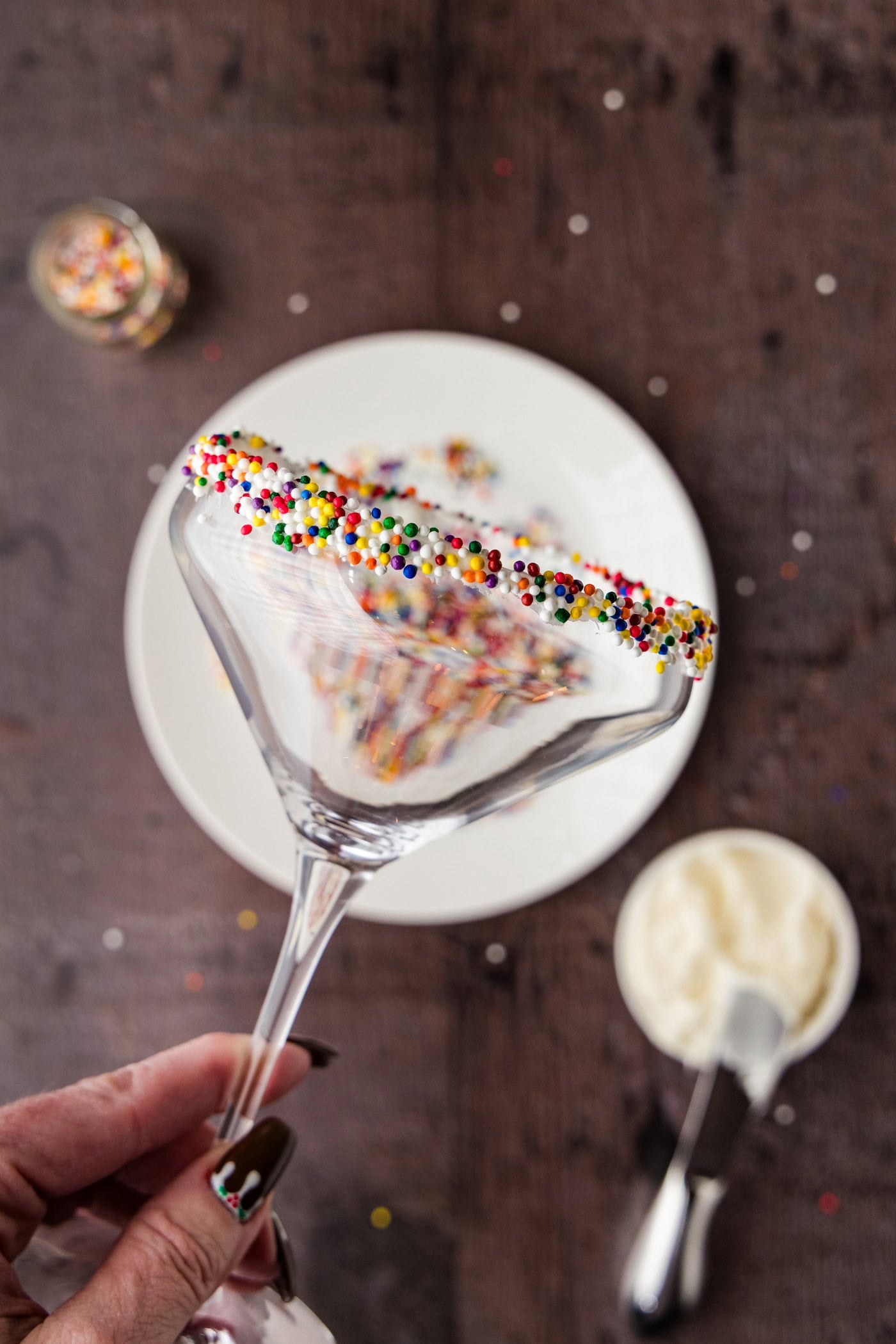 holding a martini glass with the rim coated in frosting and rolled in sprinkles