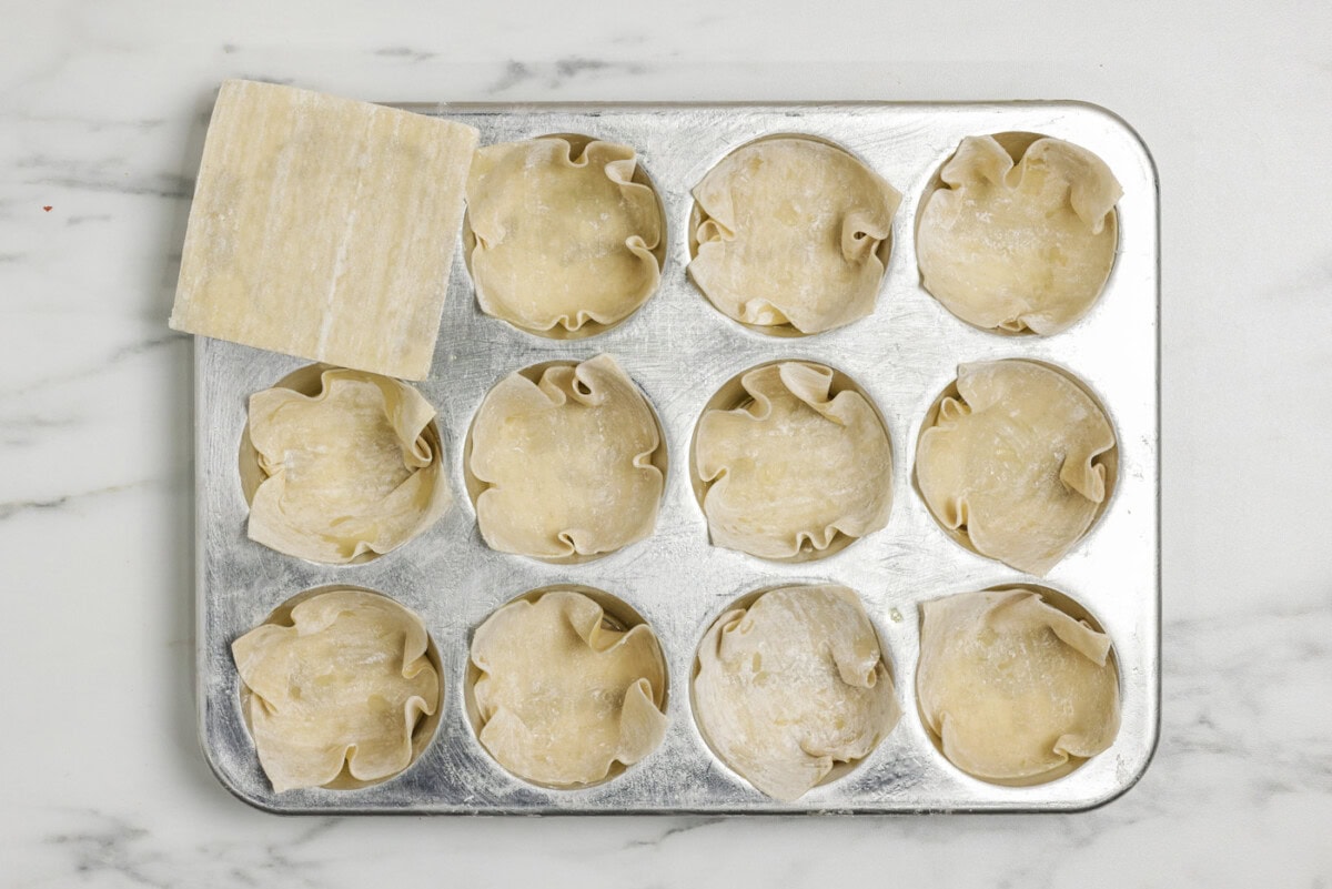 Wonton wrappers tucked inside muffin pan cavities
