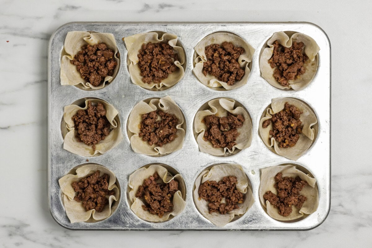 Taco meat placed inside wonton wrappers in a muffin pan
