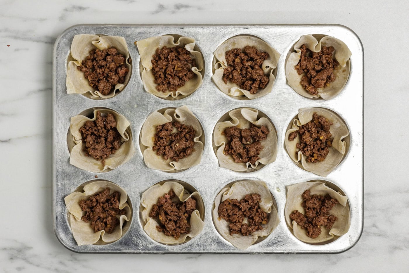 Taco meat placed inside wonton wrappers in a muffin pan
