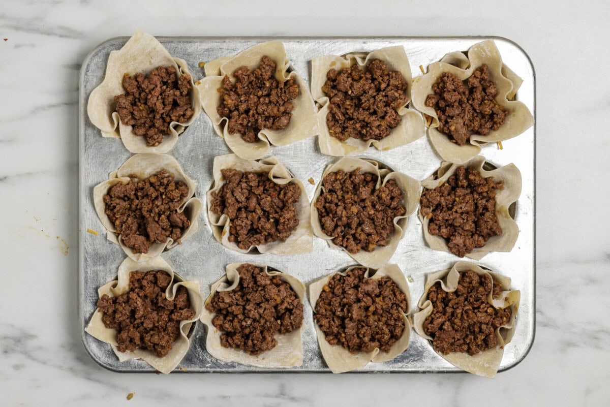 Taco meat layer overtop shredded cheese inside a wonton wrapper