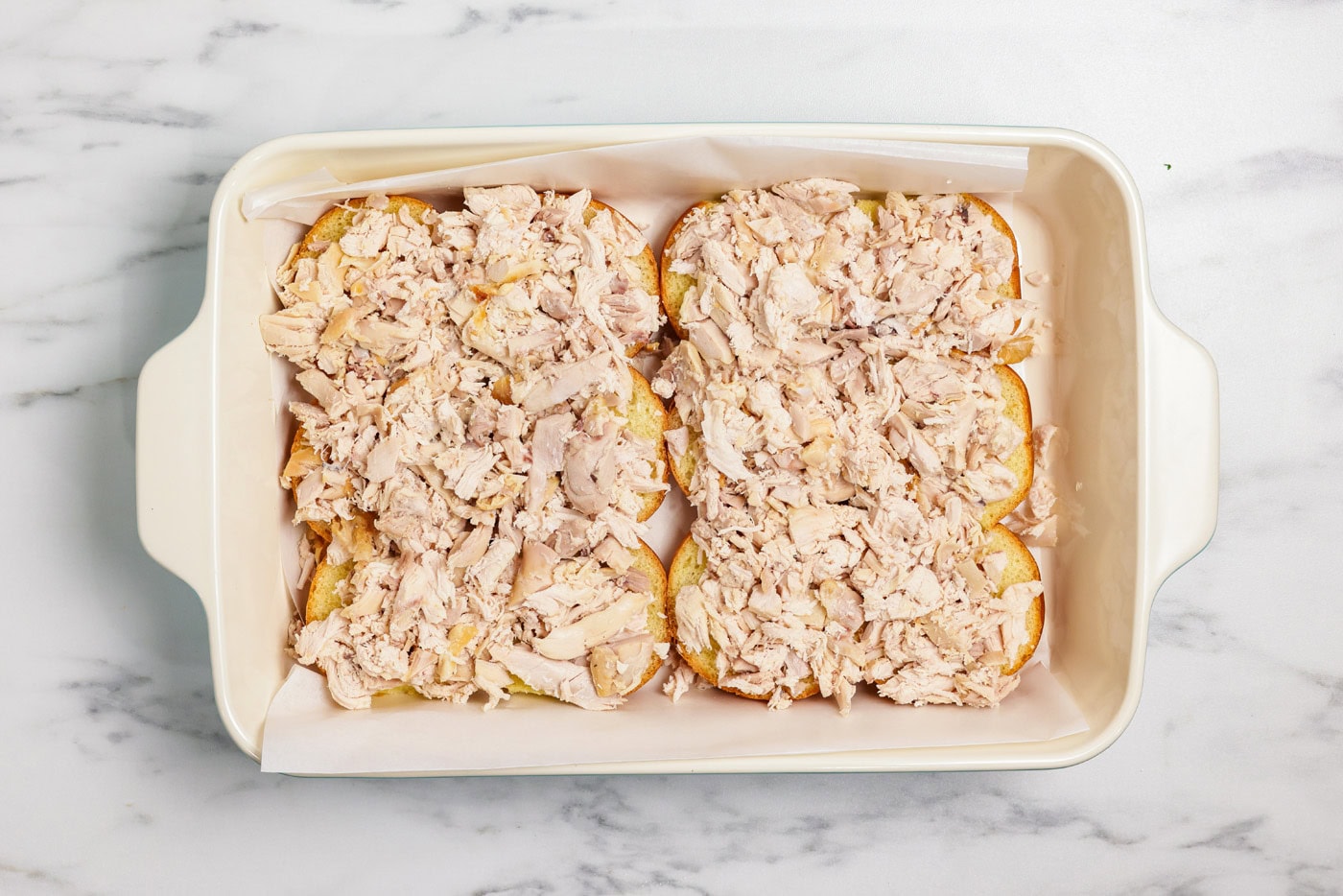 shredded chicken on top of slider buns in a baking dish