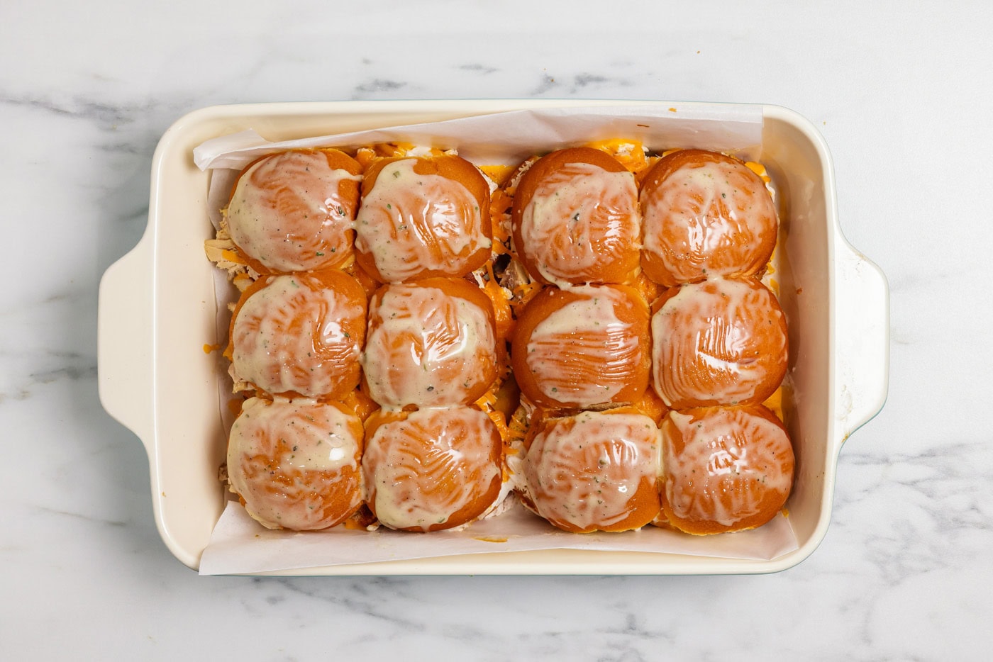 Melted butter and ranch seasoning mix basted over chicken bacon ranch sliders in a baking dish