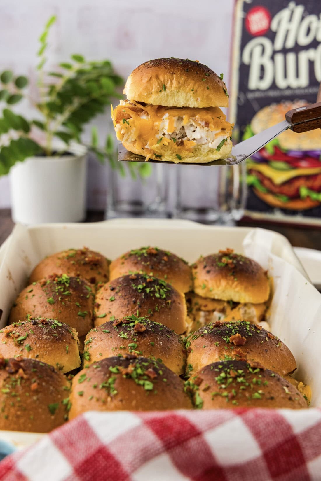 Spatula holding up a Chicken Bacon Ranch Slider above a pan of Chicken Bacon Ranch Sliders