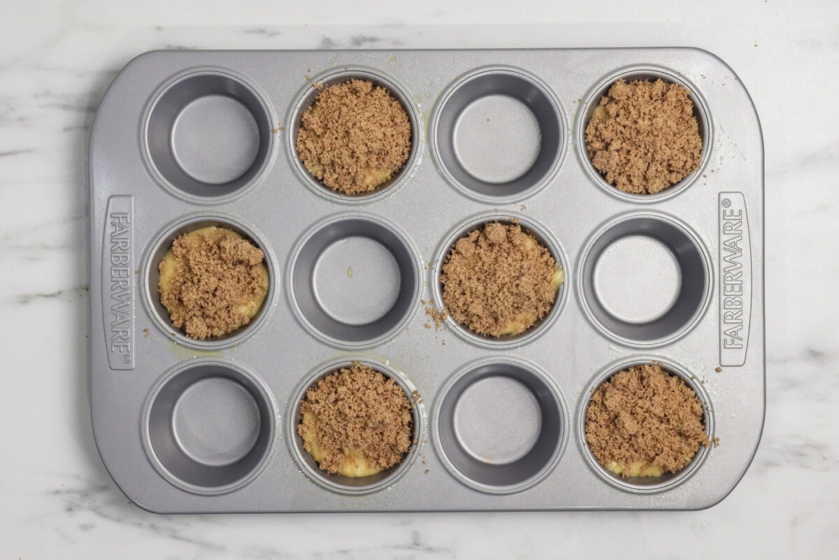 Cinnamon streusel added on top of vanilla muffin batter in a muffin pan